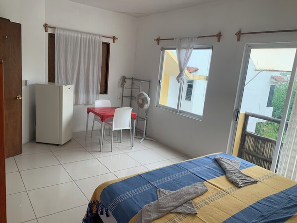 Une chambre avec un lit, un bureau et une chaise, un ventilateur et une fenêtre.