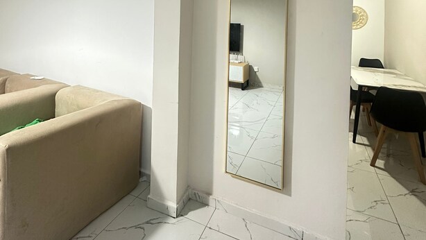 Una sala de estar minimalista con un sofá, un espejo grande y una zona de comedor con una mesa y sillas.