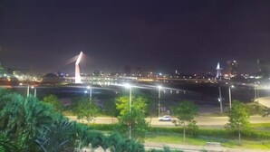 Vista nocturna de un paisaje urbano con un puente destacado y luces de la ciudad a lo lejos.
