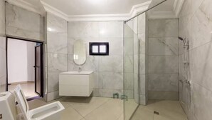 Un baño con ducha envuelta en vidrio, tocador blanco y espejo.