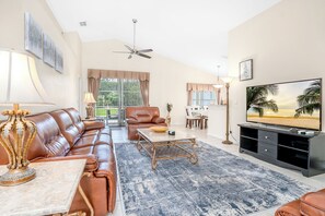A living room with a brown leather sofa, a coffee table, a TV, and a ceiling fan. - Spectacular 3b/2b With Private Pool And Spa (Davenport)