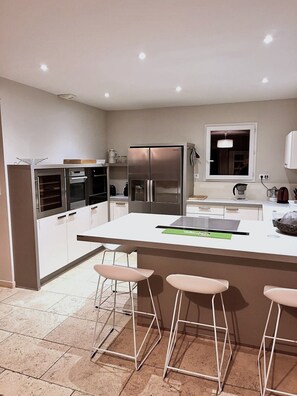 A modern kitchen with a central island, bar stools, stainless steel appliances, and a window. - Air-conditioned villa with heated pool - Golf de Pont-Royal - 6 pers (Mallemort)