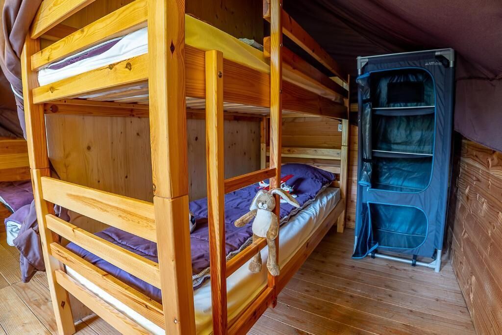 Een slaapkamer met een stapelbed, een klein tentachtig bouwwerk en een speeltje op het onderste bed.