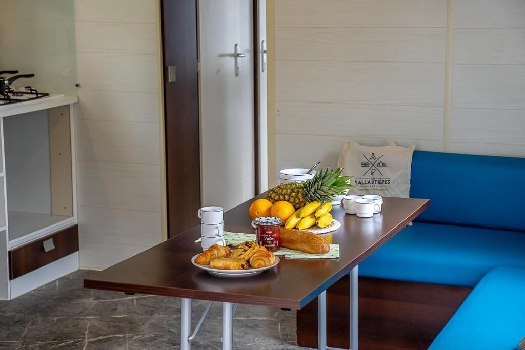 A breakfast table with croissants, bananas, oranges, a pineapple, and a bottle of jam.