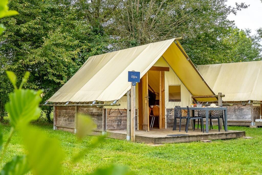 A tented accommodation with a wooden deck, a table with chairs, and a sign indicating the name and number.