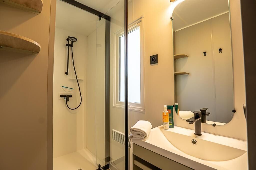 Een badkamer met een douche met glazen wand, een wastafel met spiegel en een handdoek op het aanrecht.