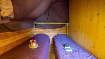 A bunk bed with purple bedding, a wooden ladder, and a small table with a hat and flowers.