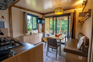 Een kleine keuken met een gasfornuis, een eettafel met stoelen, een bankje en een groot raam met gordijnen.