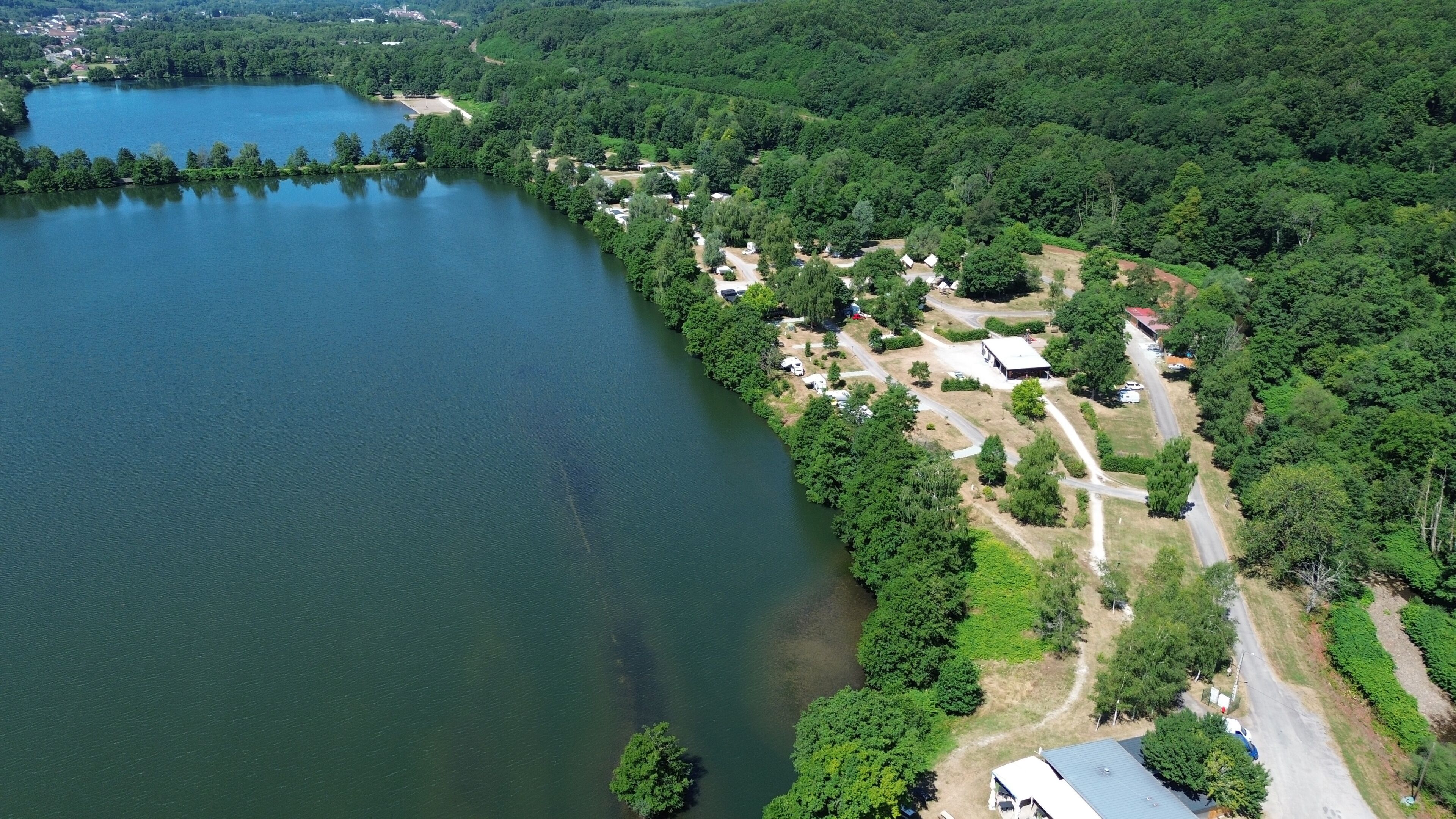 Vue aérienne d’une propriété au bord d’un lac, avec une route, des bâtiments et une forêt dense.