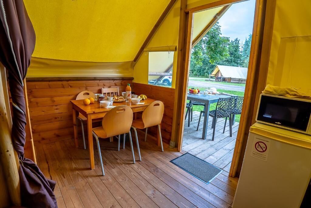 A wooden interior with a dining table, chairs, a refrigerator, and a view of the outside.