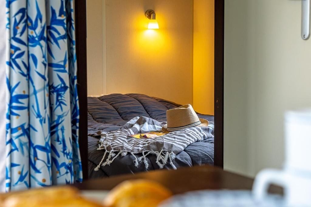 A hotel room with a bed, a wall-mounted light, and a curtain with a blue pattern.
