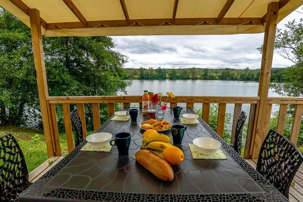 Uma área de refeições coberta ao ar livre, com uma mesa posta para o café da manhã, com vista para um lago.