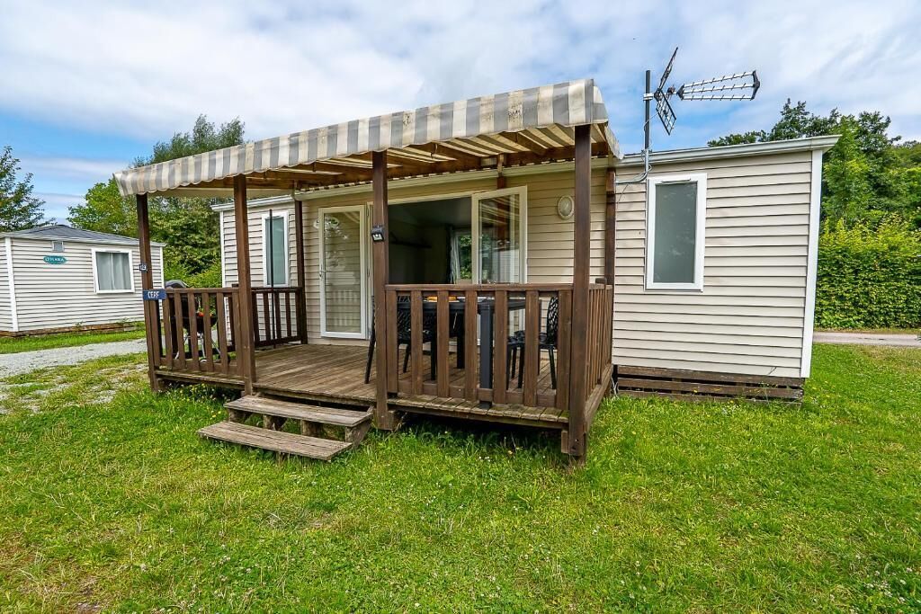 A mobile home with a wooden porch and a small deck, surrounded by grass and other mobile homes.