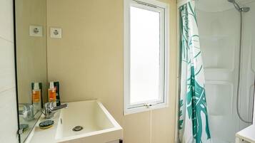 A bathroom with a sink, mirror, window, shower, and a green leaf-patterned shower curtain.
