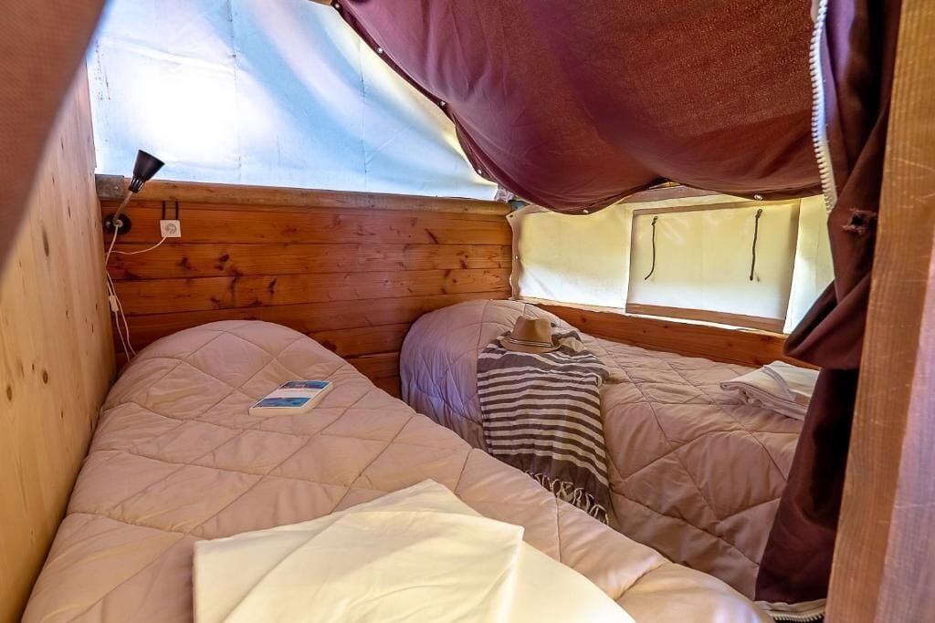 A tented accommodation with two beds, a window, and a power outlet.
