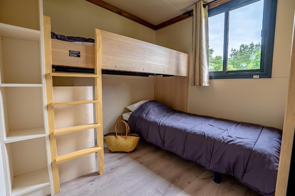 Ein kleines Zimmer mit Etagenbett, einer Holzleiter, einem kleinen Korb und einem Fenster mit Blick auf Bäume.