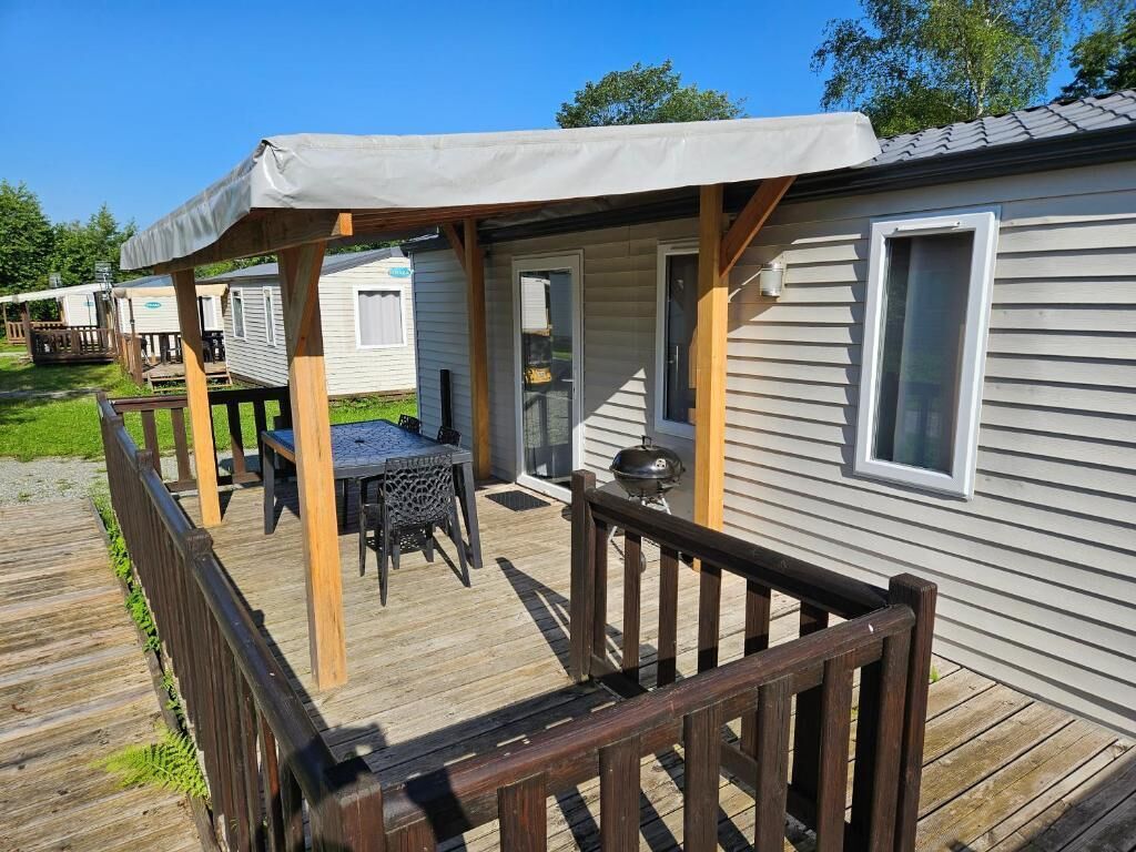 A mobile home with a covered porch, a barbecue grill, and a table with chairs.