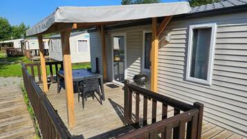 A mobile home with a covered porch, a barbecue grill, and a table with chairs.