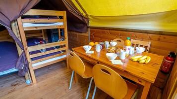 A tented accommodation with bunk beds, a wooden table with breakfast items, and a fire extinguisher.