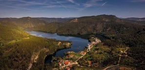 A lake surrounded by forested hills, a small village with buildings, and a clear sky.