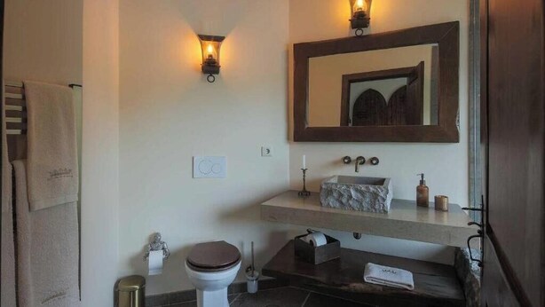 Ein Badezimmer mit Toilette, Waschbecken, Spiegel, Handtuchhalter und Mülleimer.