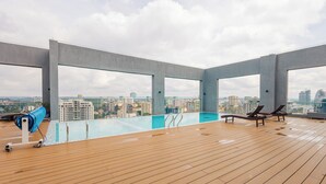 Une piscine sur le toit offrant une vue dégagée sur les gratte-ciel de la ville, des chaises longues et un fauteuil de massage.