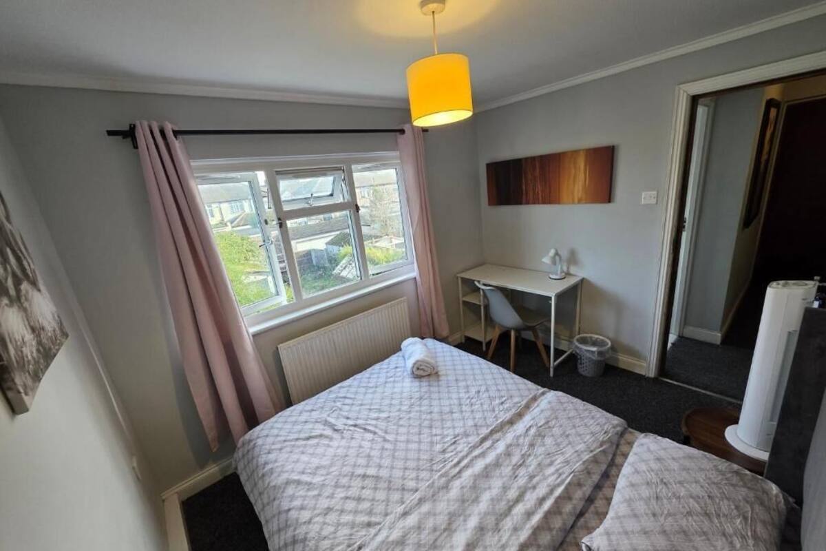 A bedroom with a bed, a desk, a chair, a window with curtains, and a ceiling light.