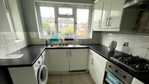 A compact kitchen with a washing machine, a stove, and cabinets. - Fenia Estate (Barking)