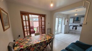 A dining area with a table covered in a fruit quilt, a sofa, and a kitchen in the background. - Fenia Estate (Barking)