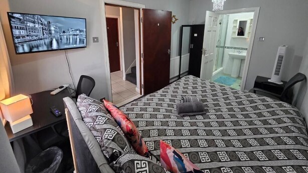 A hotel room with a bed, a desk, a TV, a chandelier, and a bathroom. - Fenia Estate (Barking)