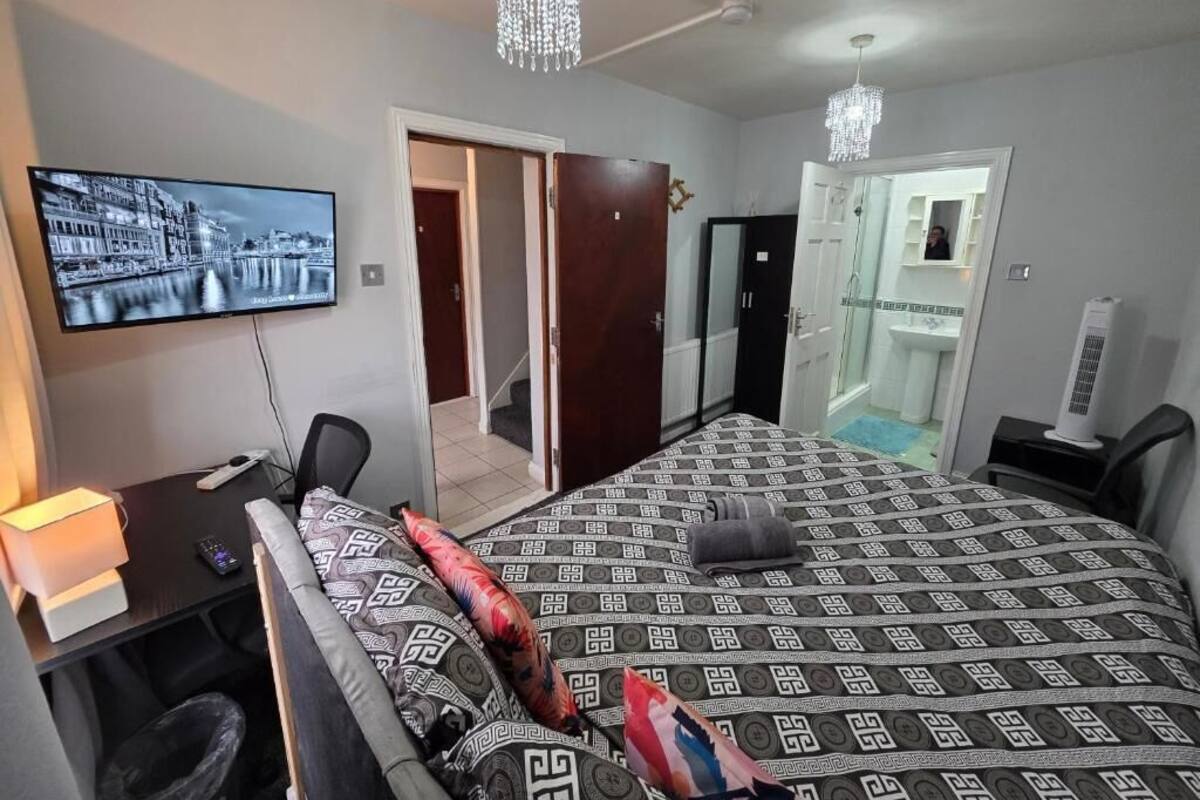 A hotel room with a bed, a desk, a TV, a chandelier, and a bathroom.
