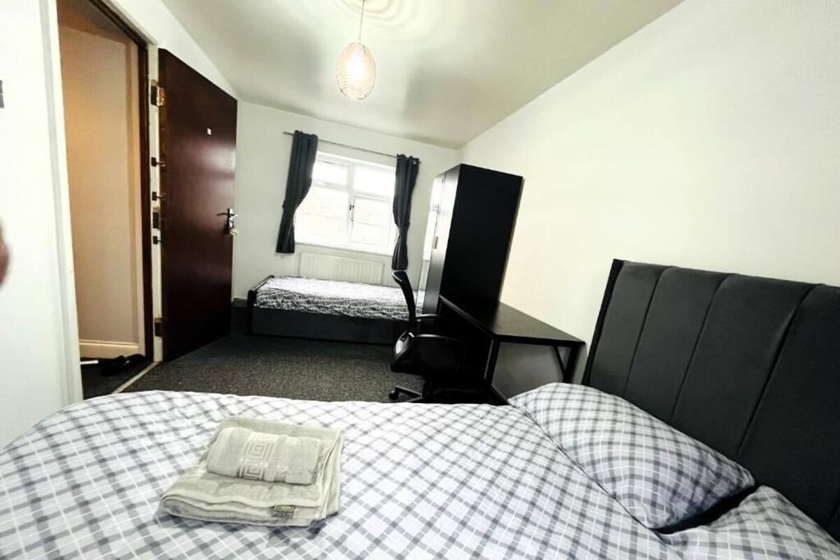 A bedroom with a bed, a desk, a chair, a wardrobe, and a window with curtains.