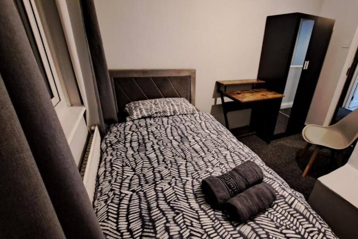 A small, narrow hotel room with a bed, a desk, a chair, and a wardrobe.