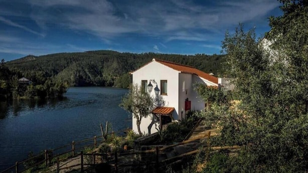 Un edificio blanco con techo rojo junto a un lago, rodeado de árboles y colinas.