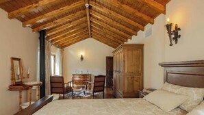 Un dormitorio con techo de madera, una cama con ropa de cama estampada, un aparador de madera y una silla.