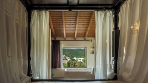 Un dormitorio con un ventanal grande, cortinas, techo de madera y una cama.