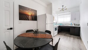 A modern kitchen with white cabinets, a black countertop, and a window with blinds. - Drexel Apts by At Mine Hospitality (Miami Beach)