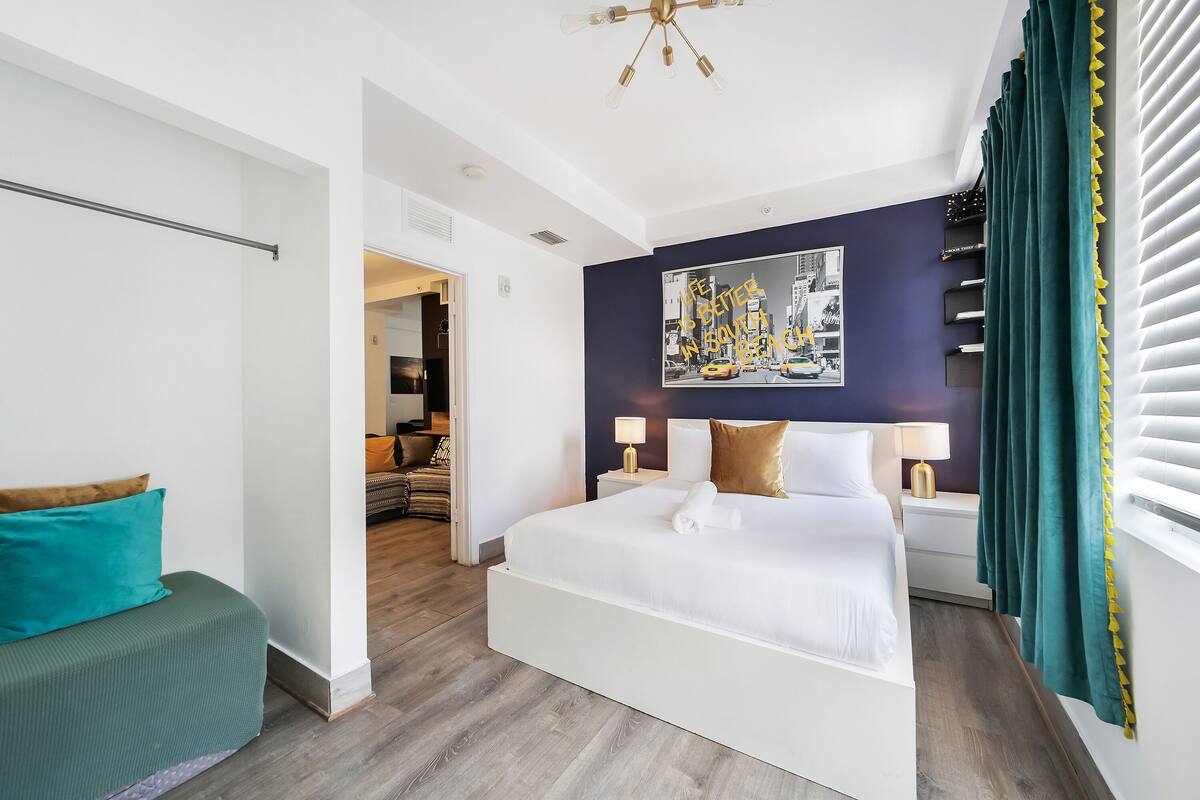 A modern hotel room with a large bed, a seating area, a painting on the wall, and a window with curtains.