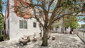 A tree-lined courtyard with outdoor seating and a building with a white facade and red accents. - Drexel Apts by At Mine Hospitality (Miami Beach)