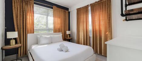 A hotel room with a large bed, two bedside tables with lamps, and curtains.