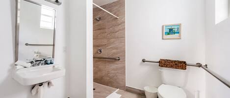Un bagno moderno con lavandino, specchio, doccia, toilette e una piccola foto incorniciata appesa al muro.