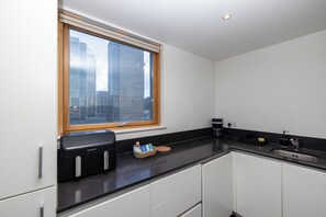 Een moderne keuken met een ingebouwde koffiezetapparaat, een raam met uitzicht op hoge gebouwen en een zwart aanrecht.