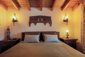 Une chambre avec un plafond en bois, un lit avec deux oreillers, deux tables de chevet avec des lampes et un élément décoratif mural au-dessus du lit.