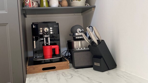 Et køkken med kaffemaskine, bestik og dekorative genstande på hylder.
