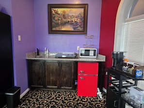 A compact kitchen with a microwave, red refrigerator, and a painting on the wall.