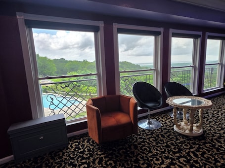 A room with a view of a pool and greenery, a brown armchair, two black chairs, a small table, and a dark patterned carpet.. Dallas Studio spectacular views-EPIC, Six Flag, Globe Life FIFA AT&T Stadium DFW
