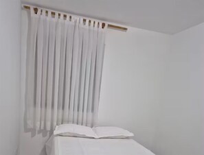 Ein Zimmer mit einem Bett, weißen Vorhängen und einem hölzernen Kopfstück.
