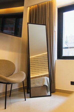 Ein Zimmer mit einem Bett, einem Sessel, einem großen Spiegel und einem Fenster mit Vorhängen.