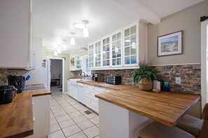 Eine Küche mit weißen Schränken, einer Holzausziehtafel und einem gefliesten Boden.