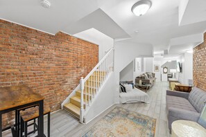 Ein geräumiges Loft mit Backsteinwand, einer Treppe, einem Wohnbereich mit Sofa und einem Esstisch.